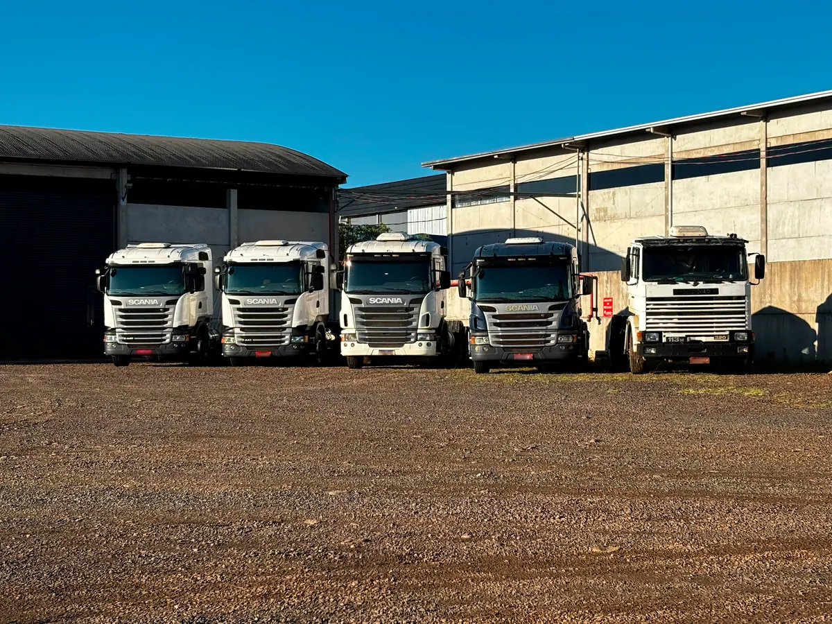 Cinco cavalos mecânicos estacionados em frente aos galpões da J3 Transportes sob céu azul